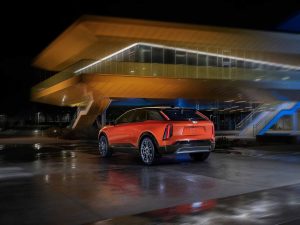 Cadillac OPTIQ 2025 diseño exterior color naranja con negro - estacionada en la noche frente a edificio con arquitectura moderna